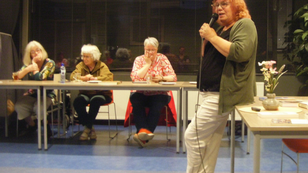 Op de foto: Ria Haan aan het woord, 3 andere vrouwen zittend aan een tafel kijken toe